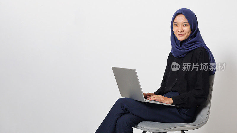 Portrait of excited Asian hijab woman in casual shirt sitting on chair, working on laptop. An employee or student doing her task and job . Businesswoman concept. Isolated image on white background